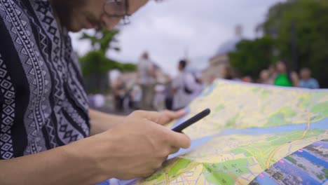 Young-man-tries-to-find-the-right-way-by-looking-at-paper-map-and-phone.